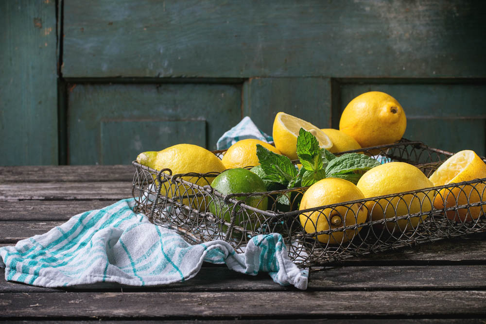 Heap of whole and sliced lemons and limes with mint in vintage metal grid box over old wooden table with turquoise wooden background. Dark rustic style.