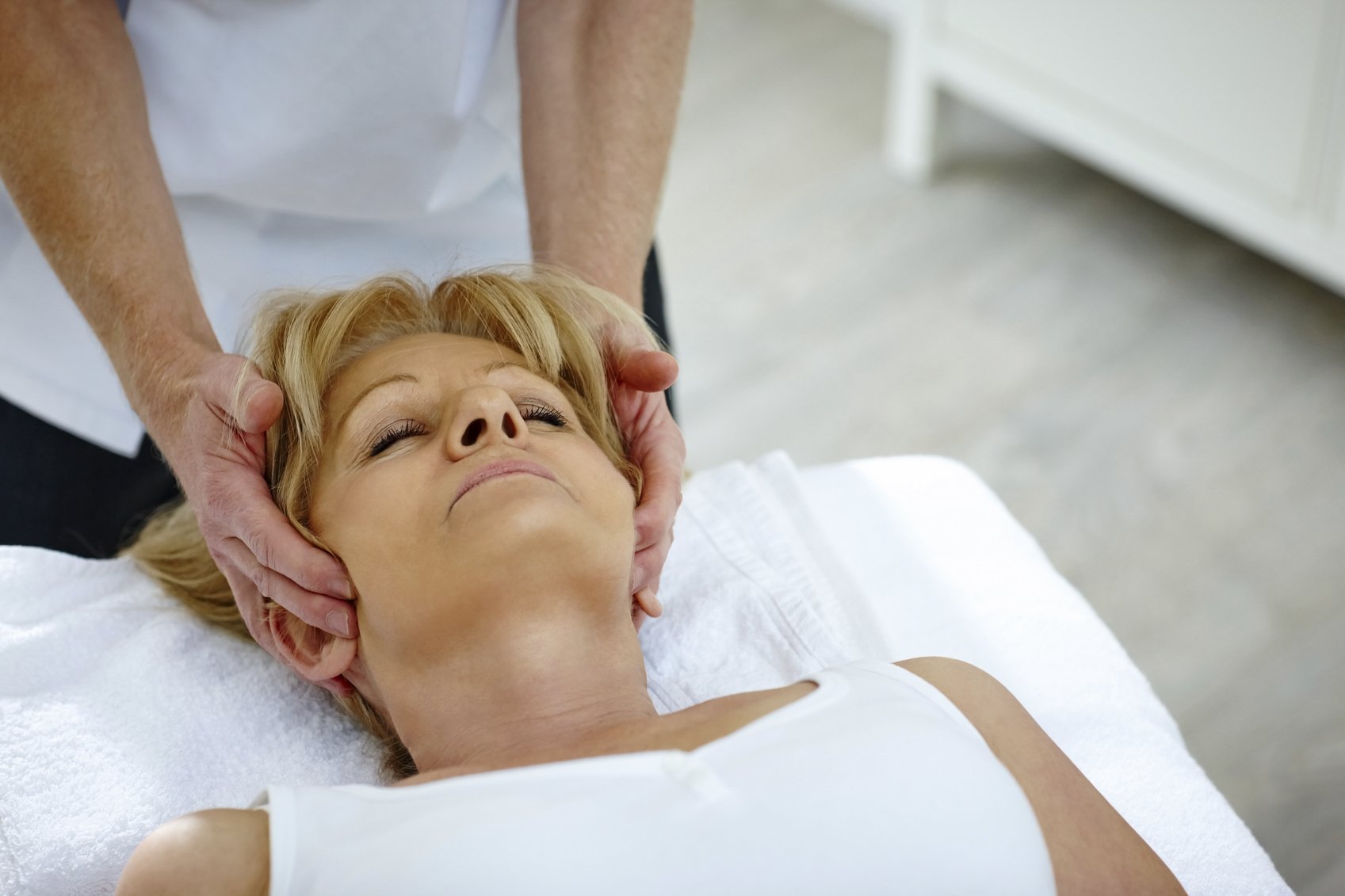 Mature woman lying on table receiving head massage from osteopath therapist