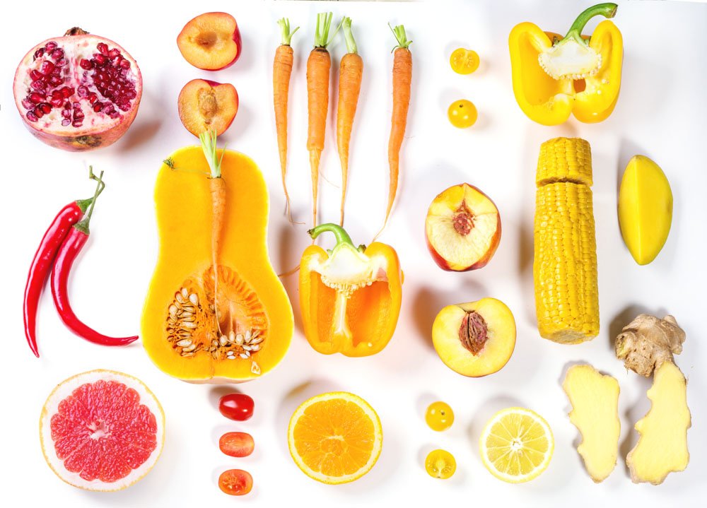 Set of whole and sliced red, orange and yellow vegetables over white background. Top view