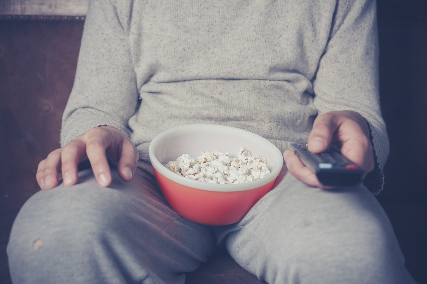 couch potato: Young man is sitting on a sofa and eating popcorn while watching television